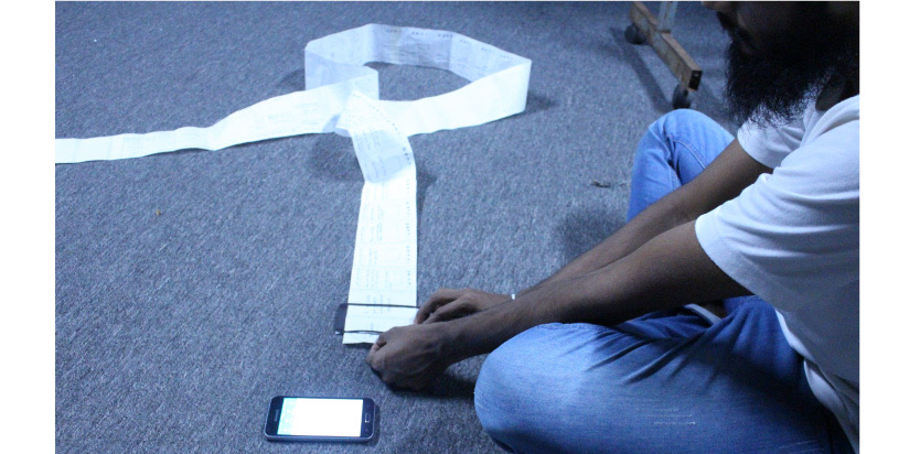 A person sitting on the floor unrolling a long strip of paper prototype next to a smartphone.