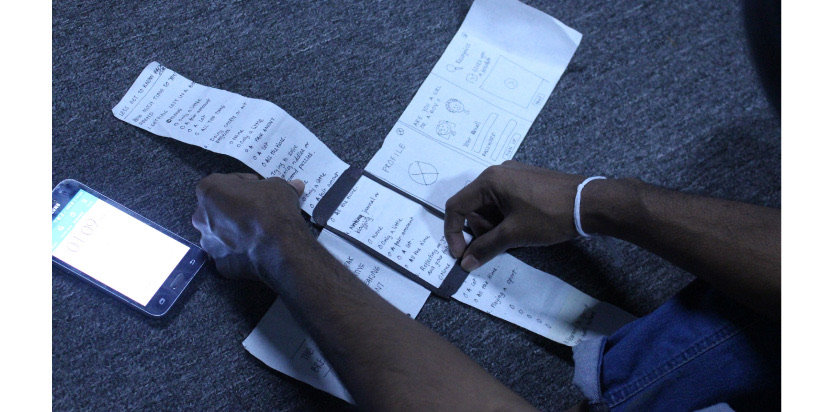 A person's hands arranging a long strip of paper with sketched screens beside a smartphone.