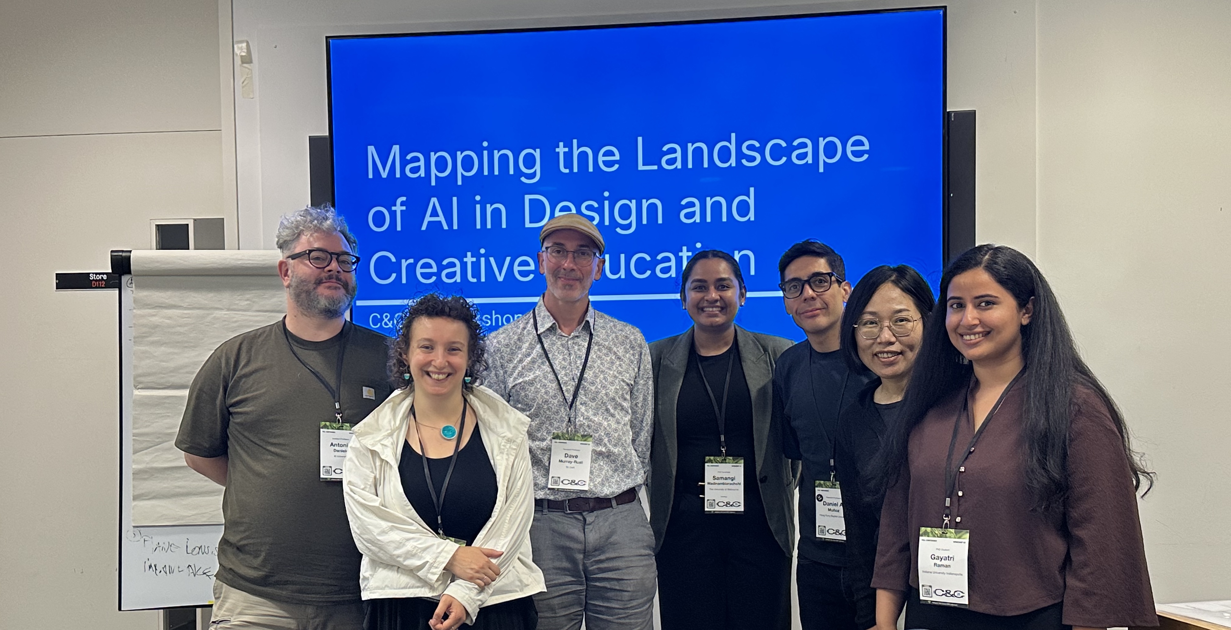 Seven workshop organisers and participants standing together in front of a screen titled Mapping the Landscape of AI in Design and Creative Education