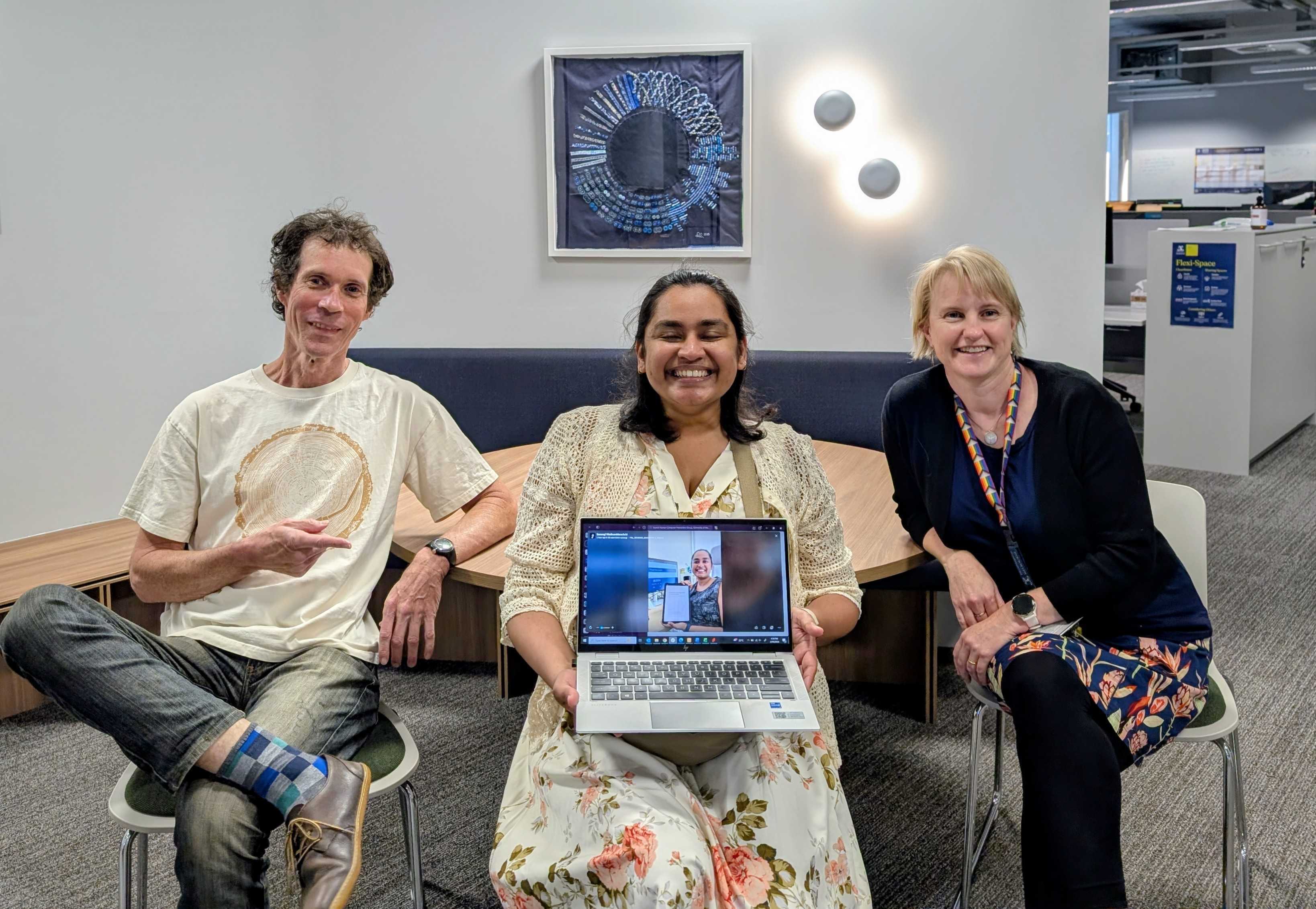 Samangi smiling in the middle of two supervisors, holding a laptop that shows a photo of the PhD testamur